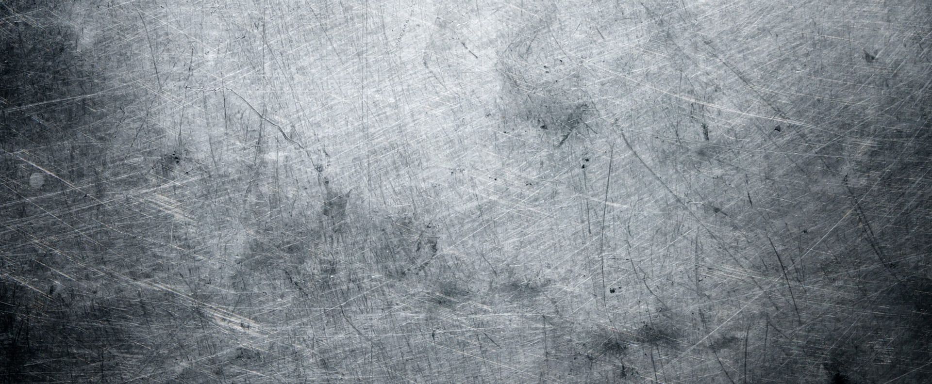 Nahaufnahme einer zerkratzten Metalloberfläche mit vielen feinen und tiefen Kratzspuren, die sich kreuz und quer über die matte, silberne Fläche verteilen.