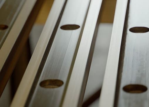 Nahaufnahme mehrerer präzise bearbeiteter Metallleisten mit runden Bohrungen, die parallel zueinander ausgerichtet sind.